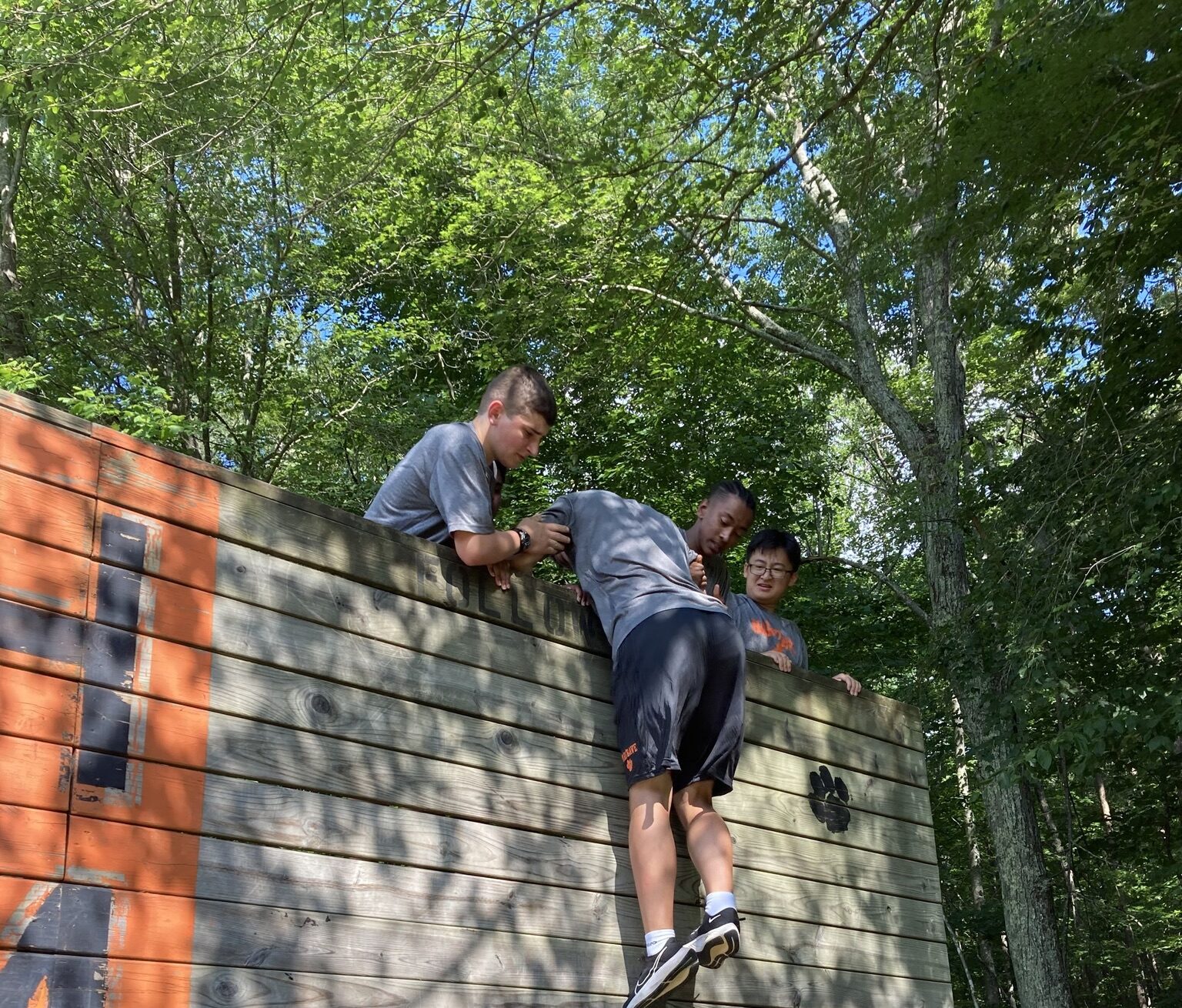 Two cadets helping another cadet over a high wall.