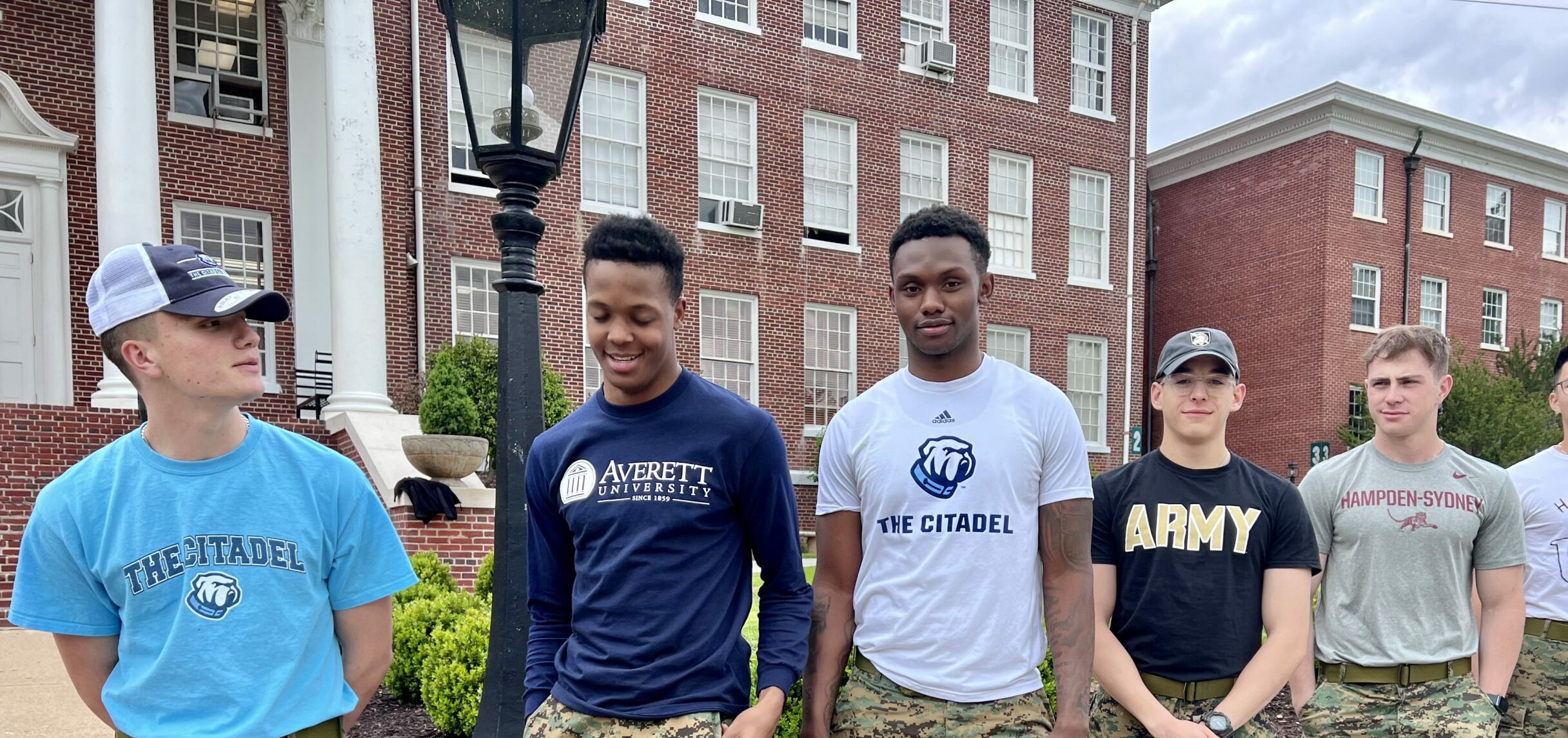 Five cadets posing in front of the school wearing their chosen college t-shirts.