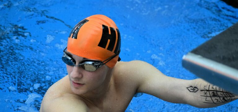 Member of swim team on starting block in pool.