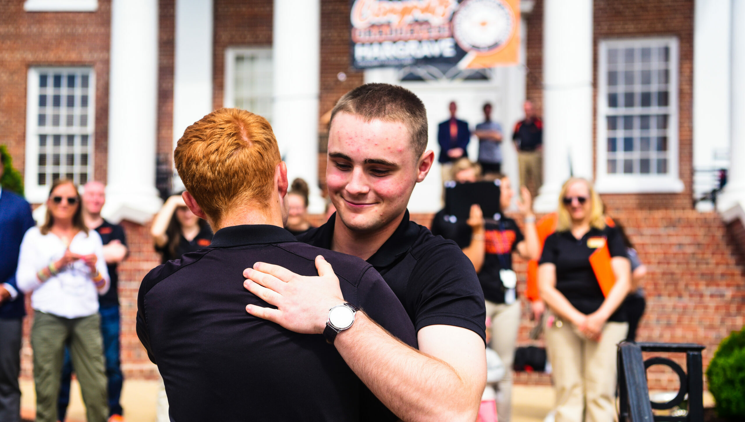 Two cadets hugging in front of main building.