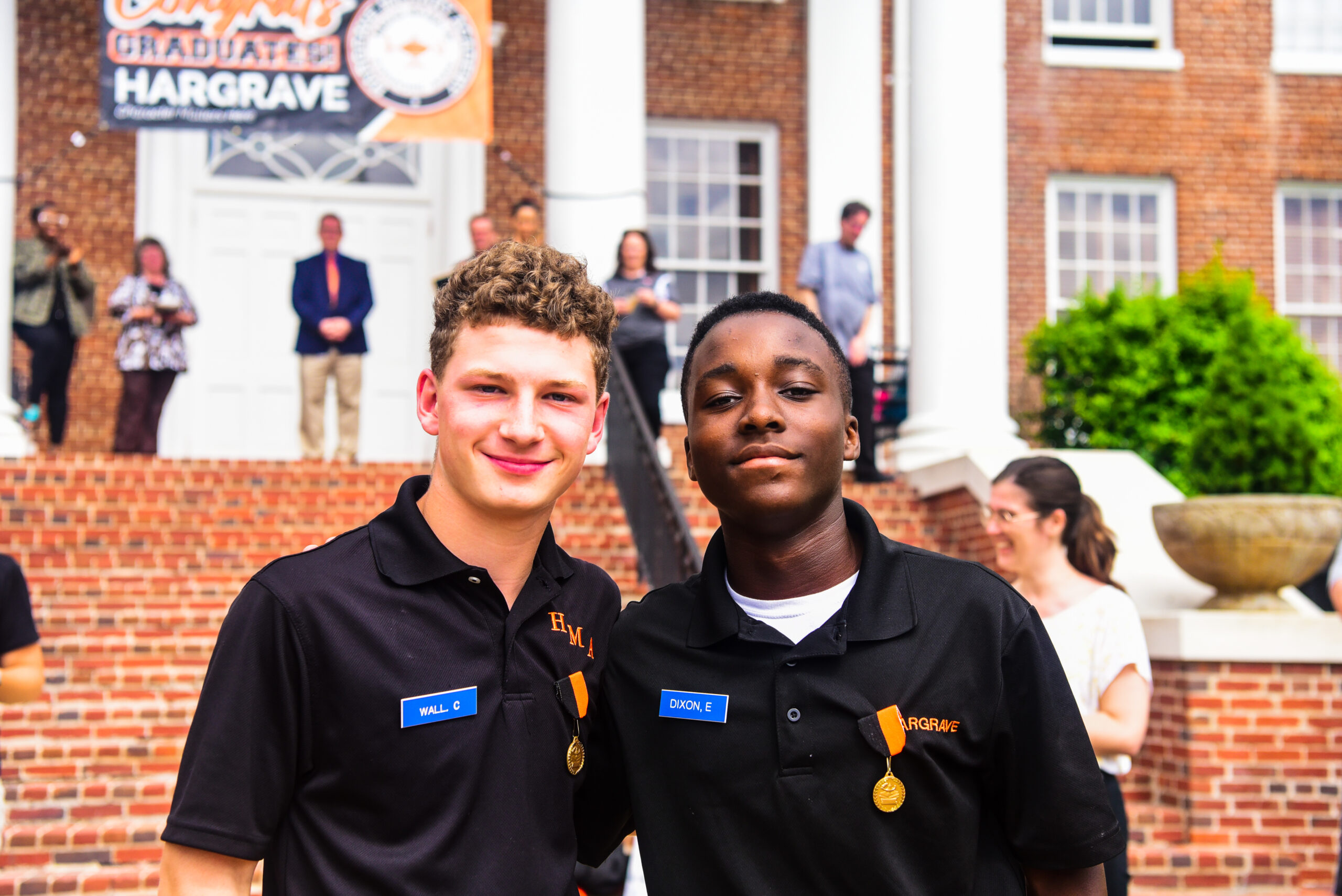 Two cadets smiling at the camera in front of the main building.